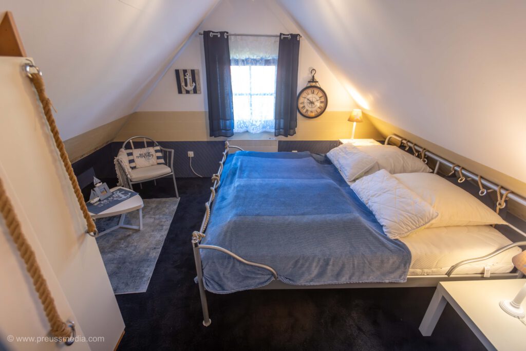 Schlafzimmer mit Doppelbett. Maritim eingerichtet mit blauen und sandfarbenen Elementen. Das Zimmer trägt den Namen Marinezimmer